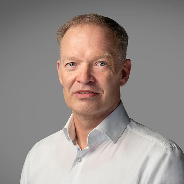 Porträt eines Mannes in einem weißen Hemd vor grauem Hintergrund.