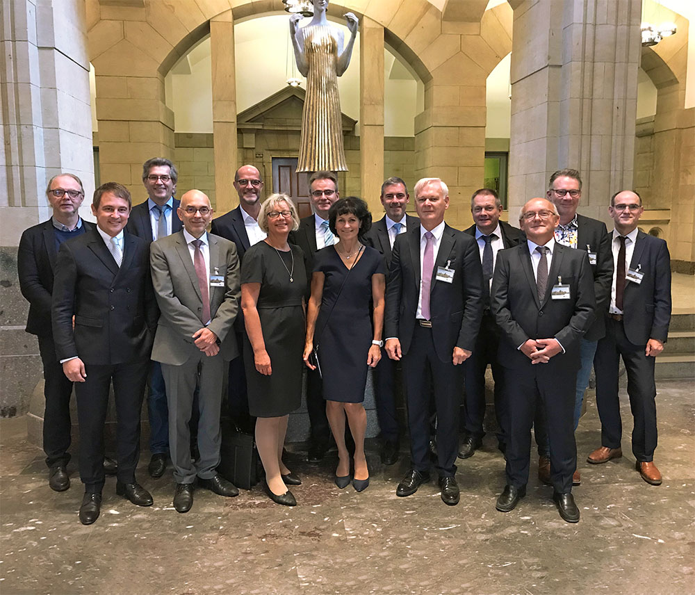 Gruppe von Personen in formeller Kleidung steht in einer Halle vor einer Statue.